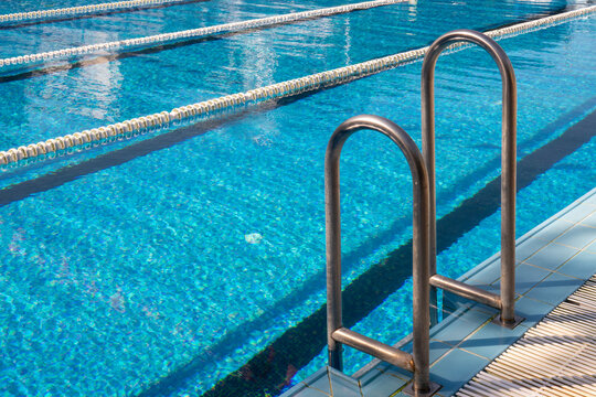 Outdoor swimming pool with clear blue water, lane lines, and a metal ladder. Detail from olympic swimming pool with swim lanes