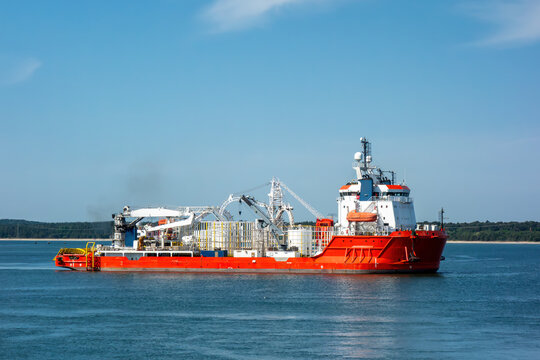 A large red cable-laying ship, an offshore construction vessel for the energy industry, sailing in the blue sea on a sunny day. Maritime logistics and subsea engineering concept.