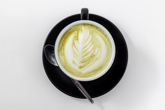 Top view of a hot matcha green tea latte with beautiful foam art in a black cup. Healthy and trendy beverage served at a cafe.