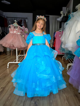 Happy little girl trying on a luxurious blue princess dress and crown in a boutique. Cute child smiling while shopping for a birthday party or special celebration.