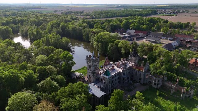Breathtaking aerial movie of the Kopice Palace ruins, a neo-Gothic residence surrounded by lush parkland and a lake, featuring monumental towers and architectural details of the historic Schaffgotsch