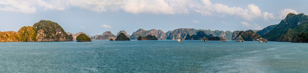 Fototapeta premium A panorama view from a cruise ship in a navigation channel passing by Karst limestone cliffs in Ha Long Bay, Vietnam illuminated by the evening light