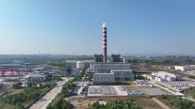 Large coal-fired power plant with red-and-white chimney emitting white steam plume under clear blue sky