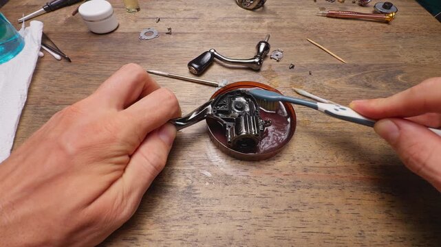 Close Up Macro Shot of Cleaning Spinning Fishing Reel Body and Gear Housing With Toothbrush in Alcohol Solution During Precision Maintenance Repair