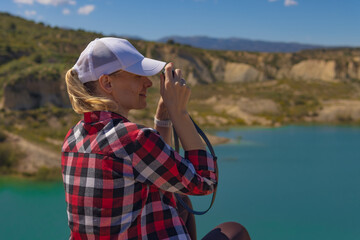 Fototapeta premium Woman traveling through nature, capturing the scenic landscape of clear blue lake and rugged mountains with vintage camera, enjoying adventure tourism and outdoor photography