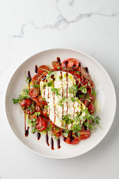 Burrata and tomato salad with balsamic glaze on a white plate