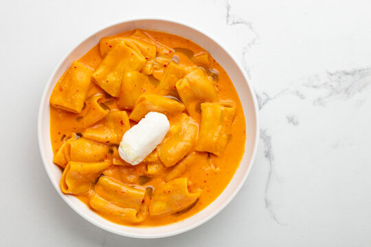 Pasta in creamy orange sauce topped with sour cream on white background