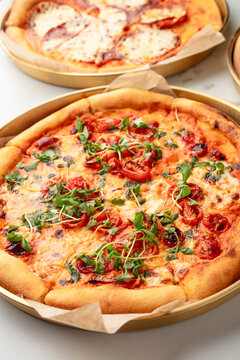 Close up of a whole pizza with melted cheese, tomato slices and herbs