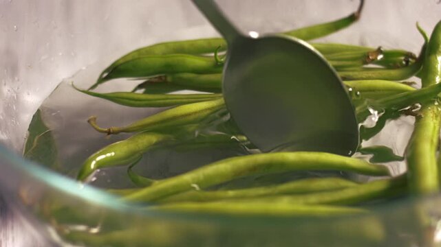 Stirring raw green beans floating in bowl of water