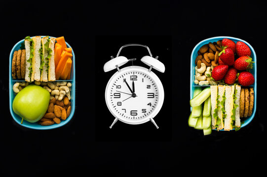 Luncn boxes and white alarm clock on a black background. Top view. Close-up.