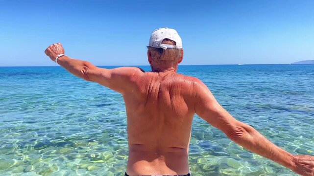 Active senior mature man doing exercise on sea beach.stretching, doing exercise in ocean coast.spreads his arms to sides.Outdoor sports training pectoral muscles,back,nature