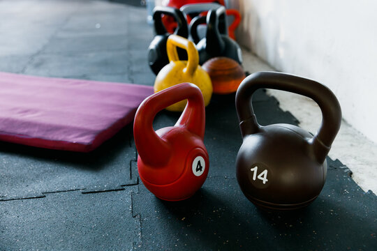 Close-up of pink 4kg and black 14kg kettlebells in a bright gym with natural light. Fitness background with copy space on the left for text. Strength training and wellness equipment concep