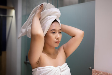 Fototapeta premium Beauty portrait of young woman with towel on head adjusting hair after shower and skincare routine. Wellness, self care, healthy lifestyle, and beauty treatment concept for cosmetic branding campaigns