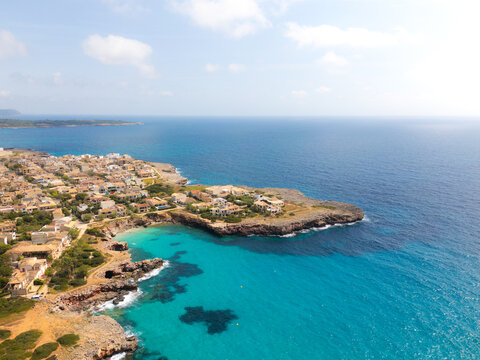 Aerial view of the turquoise waters and rocky coastline of the beach with residential buildings and lush vegetation under a bright sky Sa Coma, Balearic Islands, Spain.