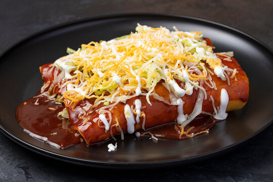 Cheese enchiladas topped with shredded cheese and sour cream on a black plate