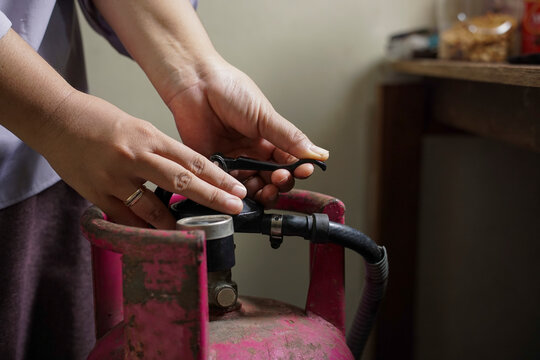 Selective focus on woman hands installing gas regulator on LPG cylinder, concept of household cooking gas and kitchen safety