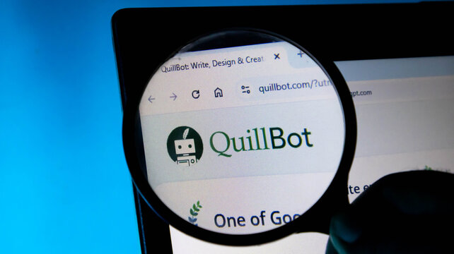 Closeup of a magnifying glass held over a screen displaying the quillbot website logo and interface, symbolizing research and writing tools