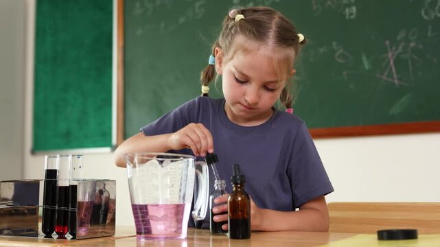 A young girl conducts a science experiment with test tubes and a dropper in a classroom setting with a chalkboard in the background.