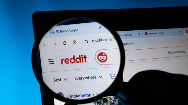 Magnifying glass focusing on reddit logo on a computer screen, social media search and investigation concept