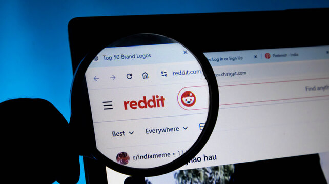 Closeup of a magnifying glass focusing on the reddit logo on a computer screen, representing digital exploration and social media research
