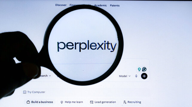 A hand holding a magnifying glass over the perplexity ai website logo on a computer screen