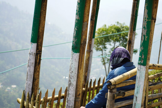 Person sitting on a bamboo bench looking out over a misty mountain valley