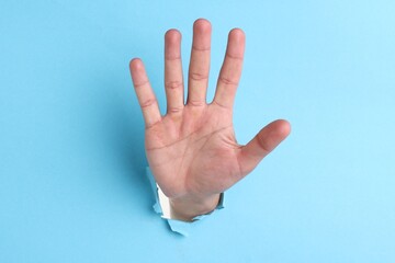 Naklejka premium Man showing palm through hole in light blue paper, closeup