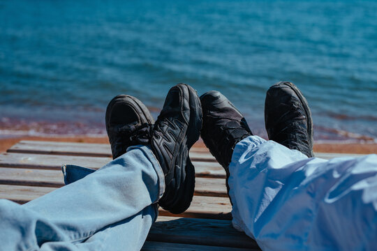 Close up of two pairs of legs in sneakers on a wooden pier