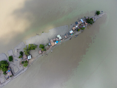 Aerial view of the narrow Kalabagi strip featuring small huts and wooden boats along the murky riverbanks in Khulna District, Khulna Division, Bangladesh.