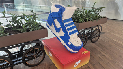 Fototapeta premium Blue and white giant Nike brick sneaker sculpture on a red pedestal, flanked by planters on wheeled carts in a modern mall. Picture taken on May 12, 2026 in Bucharest, Romania.