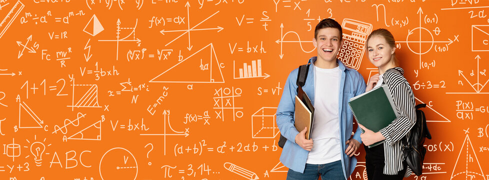 Two students stand together in front of a wall covered with math and science formulas. They hold books and smile. This scene takes place in a school environment, showcasing learning.