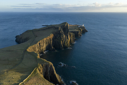 Aerial view of Neist Point Lighthouse perched on dramatic rocky cliffs overlooking the deep blue Atlantic Ocean during golden hour Isle of Skye, Scotland, United Kingdom.