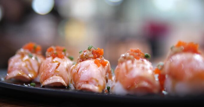 Cinematic close-up of Aburi salmon sushi topped with Ebiko (shrimp roe) on a black tray, fresh Japanese cuisine with beautiful bokeh background
