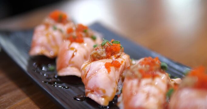 Cinematic close-up of Aburi salmon sushi topped with Ebiko (shrimp roe) on a black tray, fresh Japanese cuisine with beautiful bokeh background