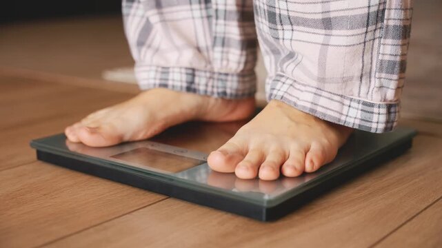 Close-up person legs bare feet stepping onto weighing scale at home. Healthy lifestyle weight awareness concept. girl weight lose standing on scales measure weight. Fitness diet BMI teen male slimming