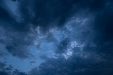 Fototapeta premium Dramatic dark storm clouds dominate a moody blue sky at dusk, creating an overcast, cinematic atmosphere that evokes tension, anticipation and the raw power of approaching weather