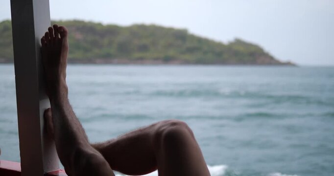 Cinematic view of a person relaxing on a boat, traveler's feet resting while cruising past a tropical island, summer vacation and serenity concept