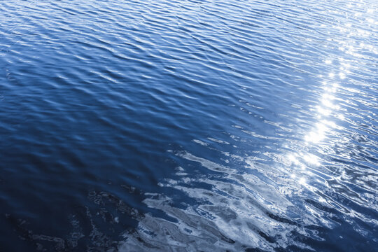 Serene closeup of deep blue water showing gentle ripples and bright sunlight reflections, conveying calm, freshness and natural texture ideal for backgrounds, design projects, wellness and environment