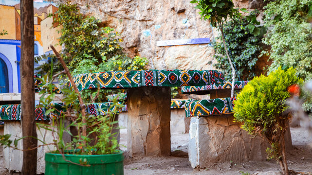 Traditional stone garden furniture with colorful Berber pattern fabrics, nestled in a shaded, flowery corner in Morocco.