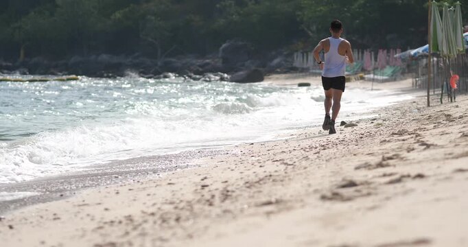 Cinematic rear view of a man in fitness wear running on a sandy beach, active lifestyle and wellness by the sea at sunny day