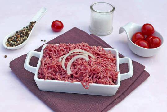  Fresh ground beef in a white baking dish with onion rings and spices.