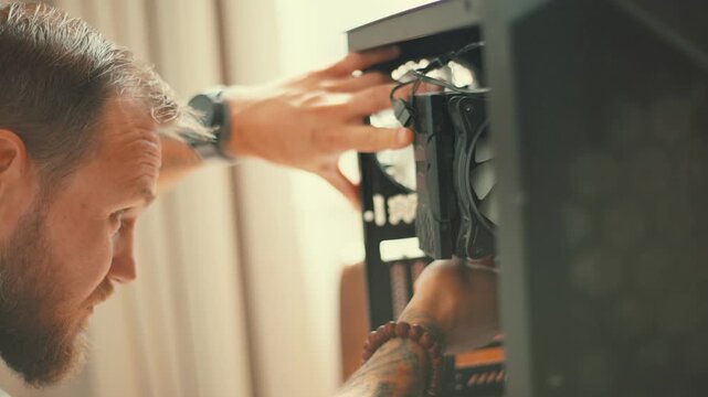 Man builds a computer in a home setting while using tools to assemble parts and connect cables