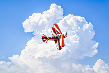 A red aerobatic biplane performing air shows in a blue sky with white clouds. Classic airplanes © Toni