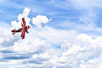 A red aerobatic biplane performing air shows in a blue sky with white clouds. Classic airplanes © Toni