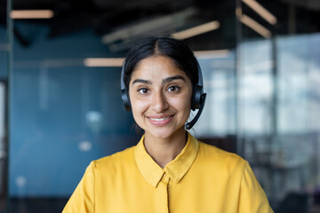 Close-up photo of a young Indian woman in a suit sitting in an office and smiling at the camera
