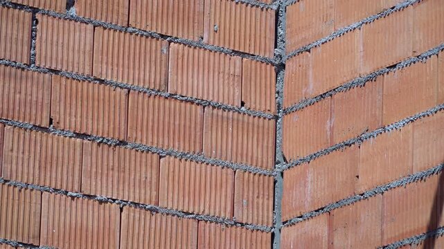 Red clay hollow bricks wall corner under construction with visible mortar layers