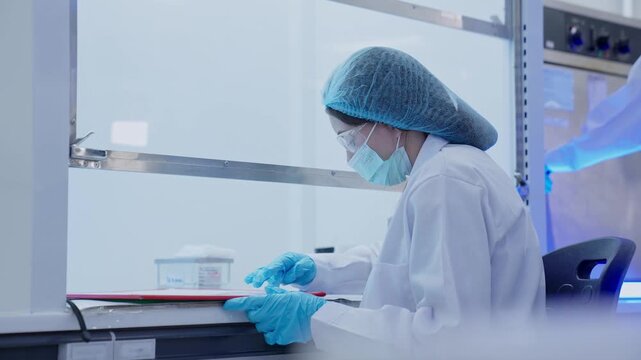 In a laboratory, a scientist in a lab coat and gloves carefully uses a pipette to transfer liquid into a dish as part of a research project. The setting is bright and organized.