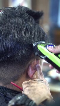 A professional barber cuts a man's hair using an electric hair clipper in a modern barbershop.