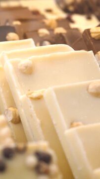 Close up view of delicious white and milk chocolate bars with hazelnuts and crispy cereals, showcasing an assortment of artisan confectionery, with the focus smoothly shifting along the rows
