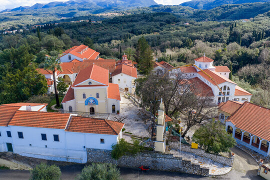 Scenic aerial landscape of Pantokrator Monastery, Agios Athanasios, Corfu. Highlighting the beautiful red-tiled roofs, courtyards, and religious architecture surrounded by dense olive groves.